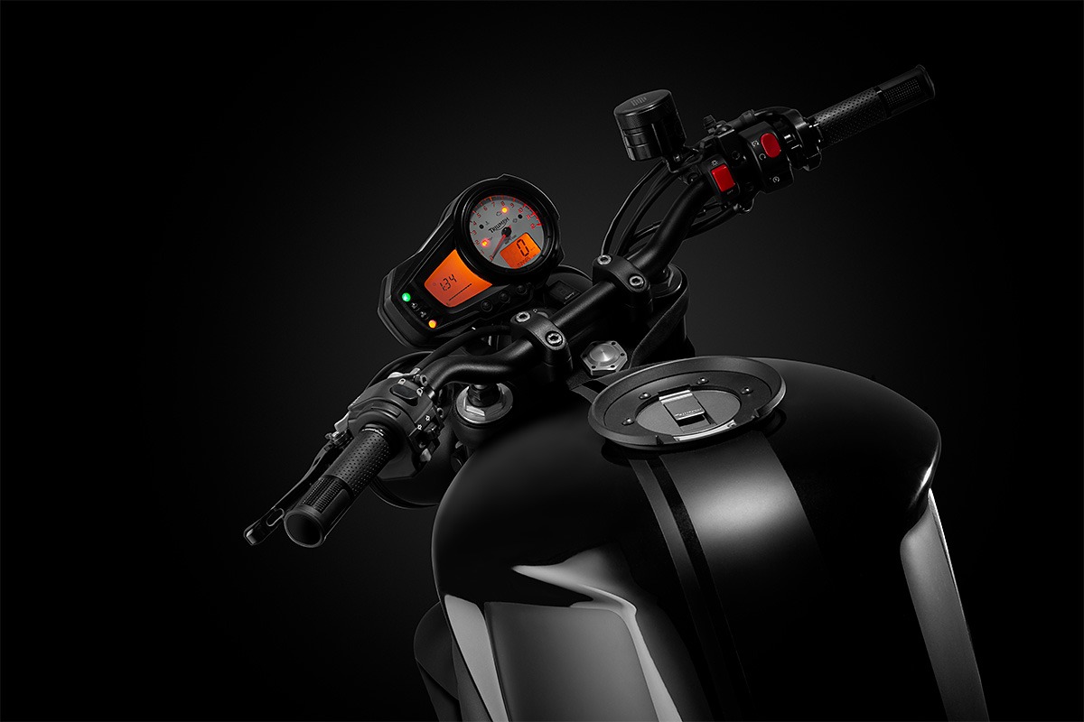 Czarny motocykl z widocznym kokpitem, kierownicą i zbiornikiem paliwa w studio z ciemnym tłem.