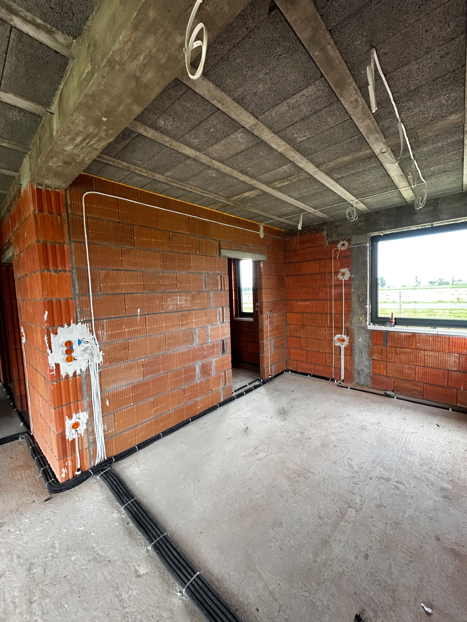 Surowy stan wnętrza z ceglanymi ścianami i betonowym stropem, widoczne kable elektryczne prowadzone wzdłuż ścian i pod sufitem, puszki instalacyjne w ścianach, przygotowane do dalszych prac...