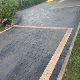 Czarno-szara kostka brukowa ułożona w kwadrat z obramowaniem z jasnej kostki, widok z góry na podjazd.