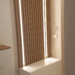 Nowoczesna aranżacja przedpokoju z drewnianymi lamelami podświetlonymi ledami, białą szafką z dwoma frontami i marmurową podłogą.