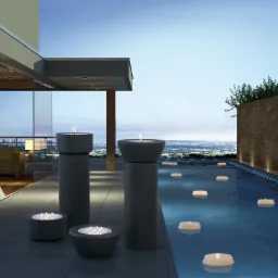 Betonowe lampiony i pływające świece w basenie na tarasie z widokiem na nocne miasto.