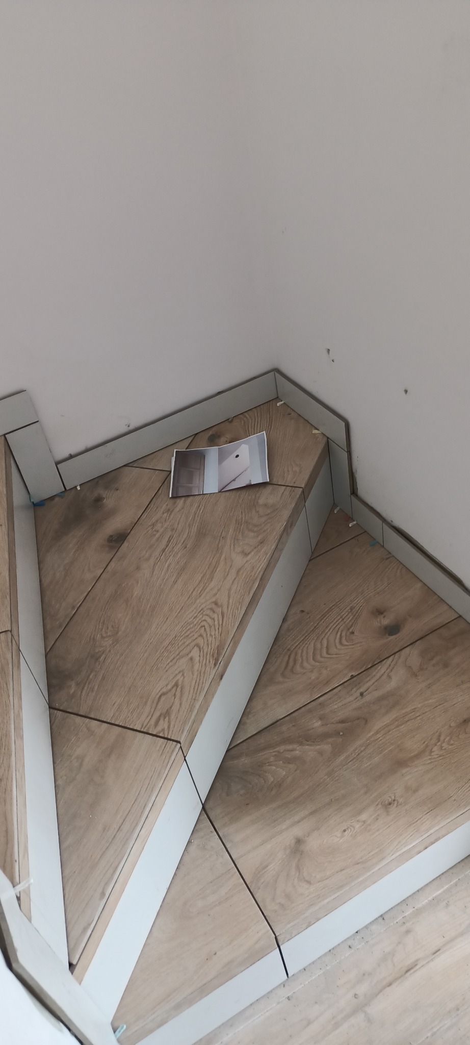 Układanie płytek imitujących drewno na schodach w Sulejówku, widoczny fragment ulotki z innym projektem.