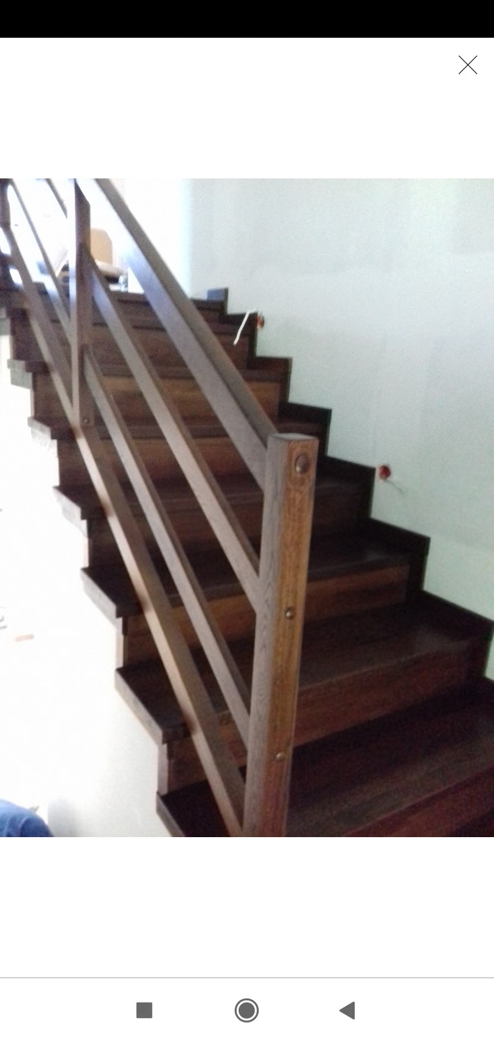 Ciemne drewniane schody z prostą balustradą z drewnianych belek, widoczne ślady po montażu na ścianie.