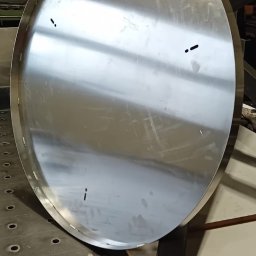 Mosqito Metal Design - Okrągły, spawany element ze stali nierdzewnej, leżący na stole spawalniczym z otworami, widoczne ślady po spawaniu punktowym.
