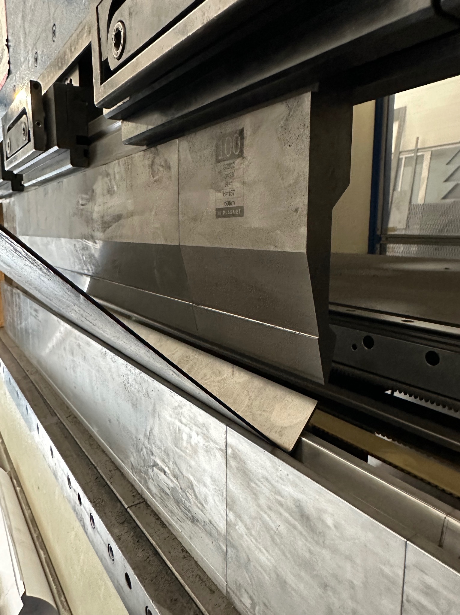 Proces gięcia blachy na prasie krawędziowej; widoczny detal z blachy pomiędzy matrycą a stemplem, maszyna z widocznymi oznaczeniami technicznymi.