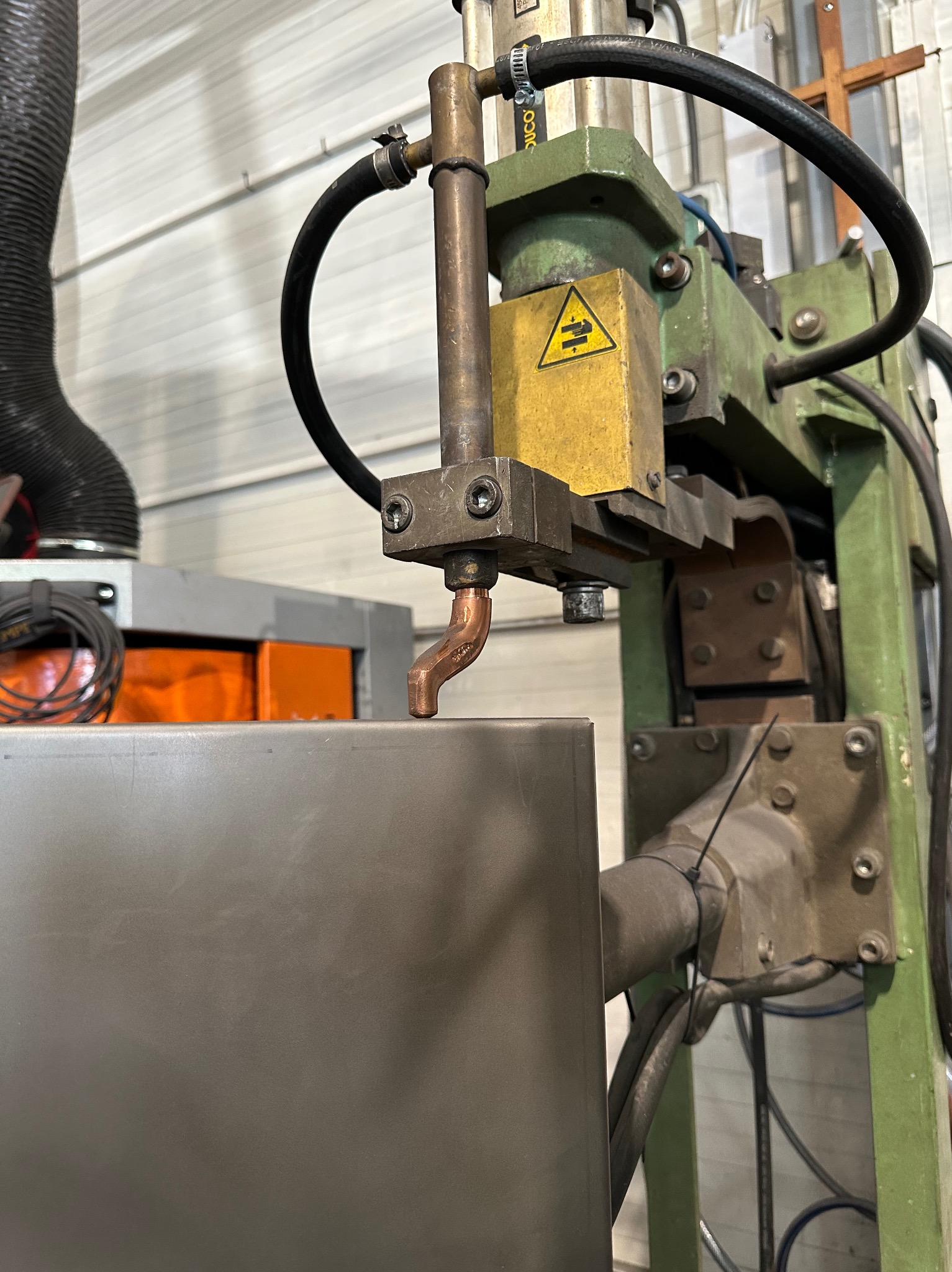 Zbliżenie na elektrodę zgrzewarki punktowej w warsztacie w Kalwarii Zebrzydowskiej, gotową do łączenia blachy. Widoczna żółta tabliczka ostrzegawcza na maszynie i fragment instalacji odpylającej.