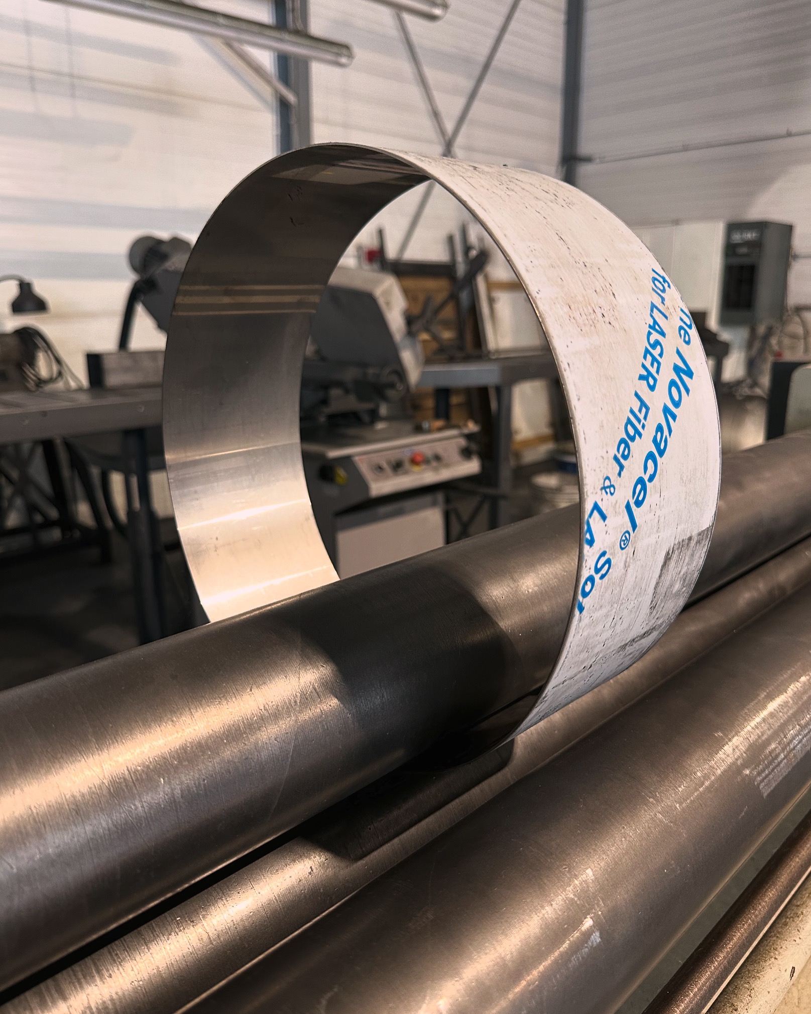 Proces gięcia blachy na walcarce trzypunktowej; widoczny fragment blachy w kształcie obręczy z folią ochronną i walce maszyny.