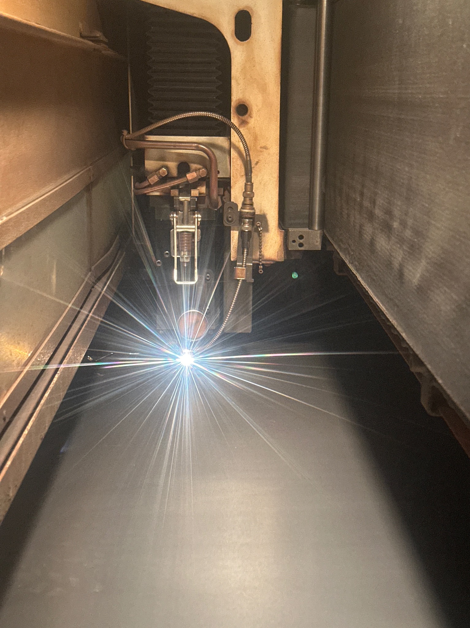 Zbliżenie na proces cięcia laserowego metalu wewnątrz maszyny, z widoczną głowicą i intensywną wiązką światła.