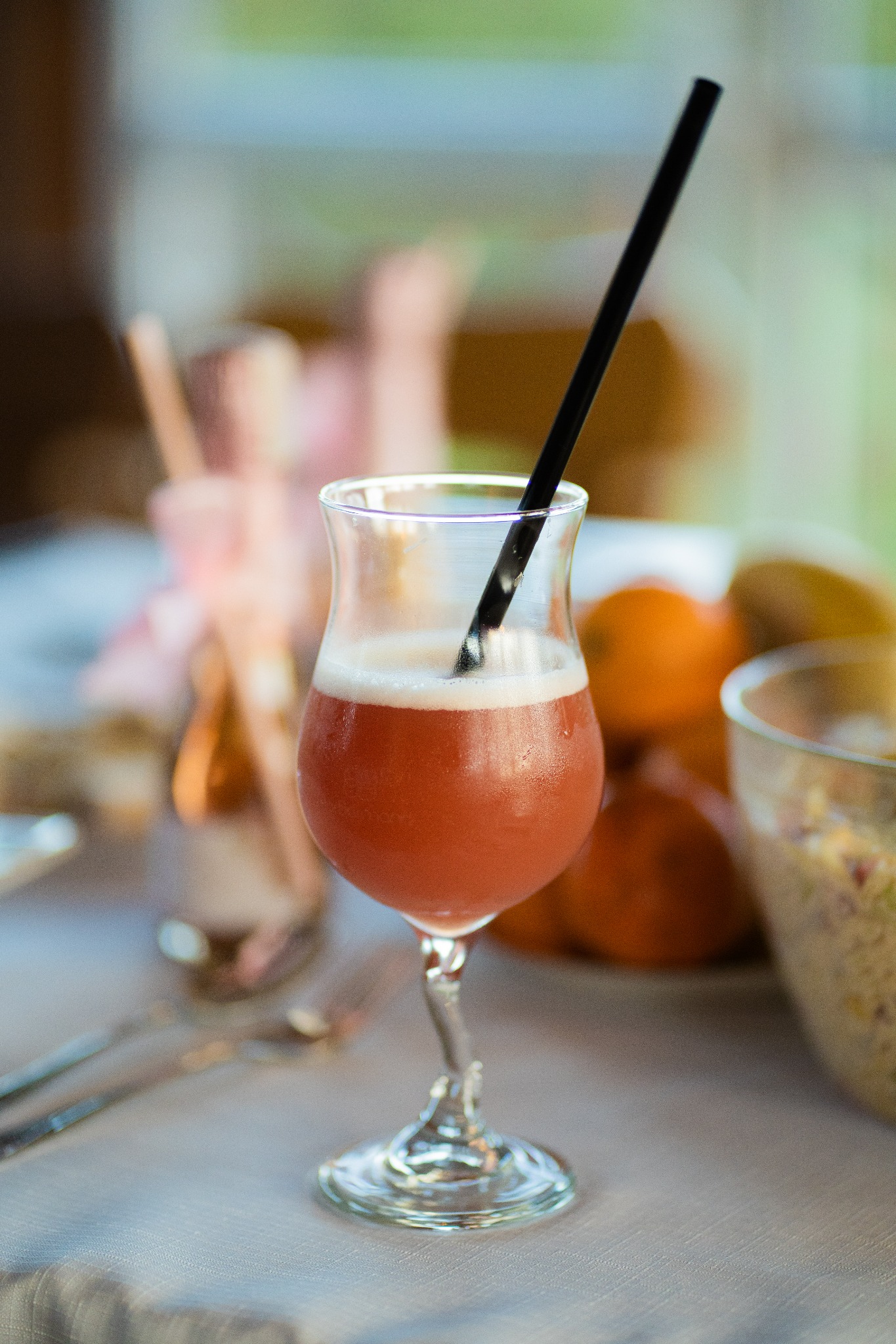 Kieliszek z różowym koktajlem z czarną słomką na stole podczas przyjęcia, w tle owoce i dekoracje.