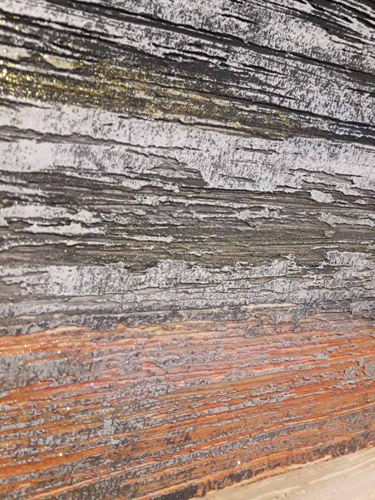 Dekoracyjna faktura ściany z poziomymi pasami w odcieniach szarości, bieli i pomarańczu, miejscami z efektem brokatu.