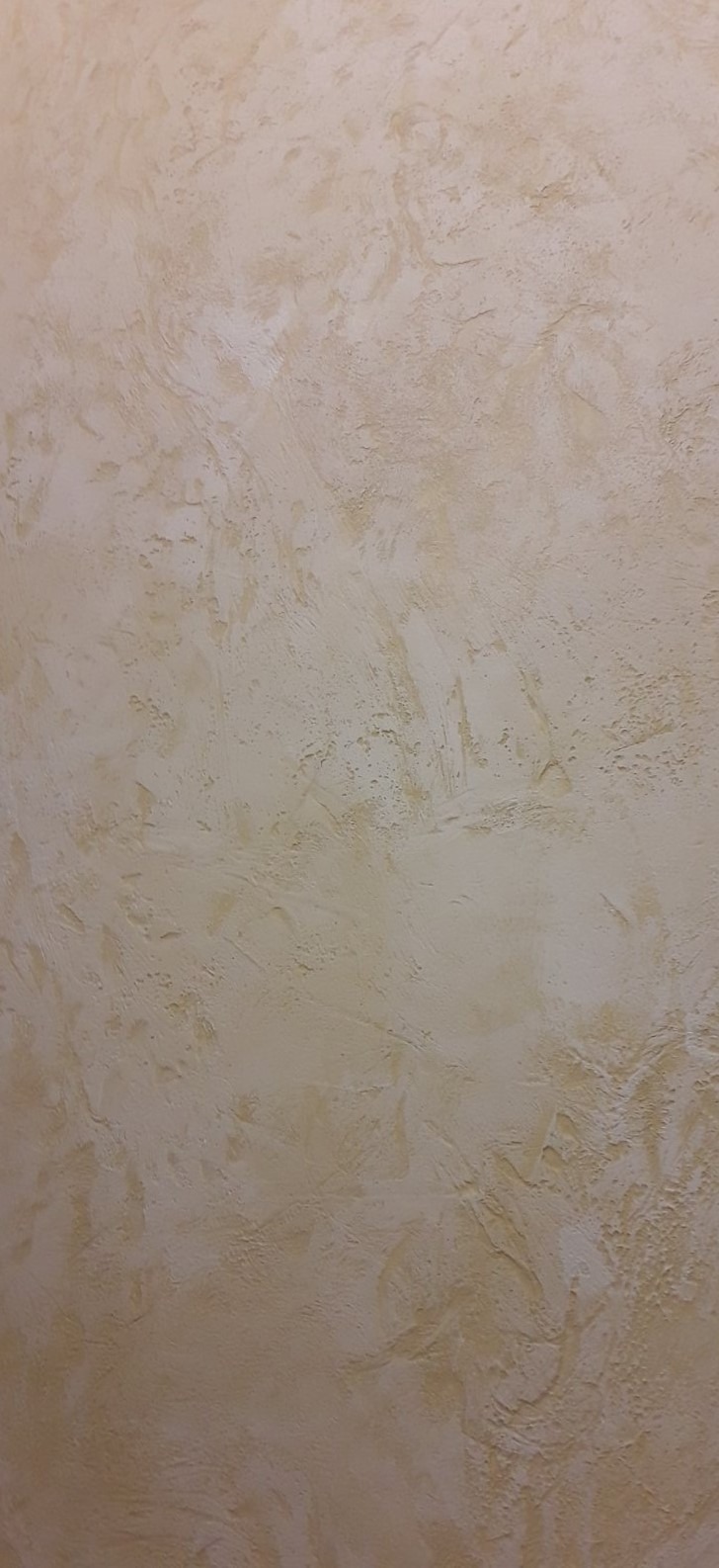 Beżowa ściana z wyraźną, nieregularną fakturą, imitująca naturalny kamień lub tynk strukturalny, oświetlona z góry, ukazująca subtelne cieniowanie i detale powierzchni.