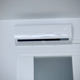 Sebastian kalinowski - Biały klimatyzator marki Nova zamontowany nad drzwiami, wyświetlający temperaturę 23 stopnie, w minimalistycznym wnętrzu.