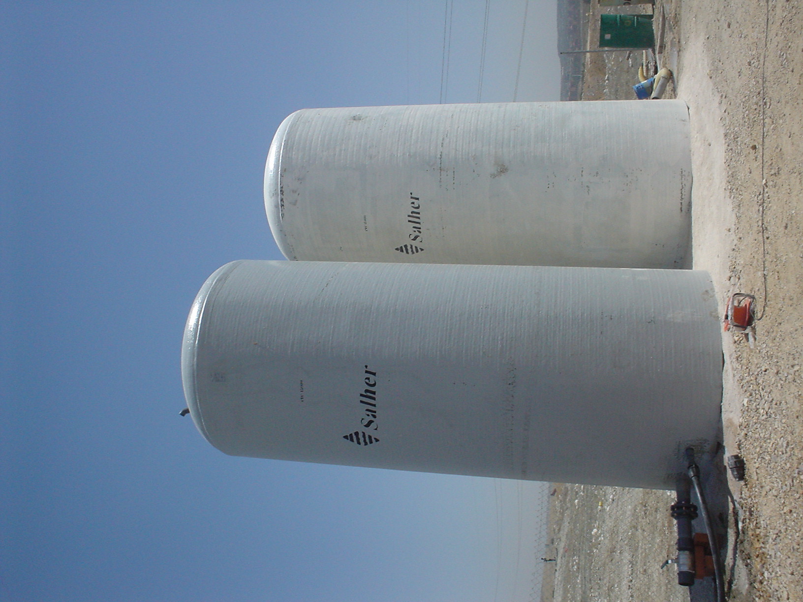 Dwa duże, cylindryczne zbiorniki z tworzywa sztucznego marki Salher, ustawione jeden za drugim na żwirowym podłożu, z widocznymi przyłączami hydraulicznymi i elementami instalacji.