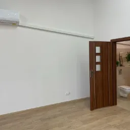 Nowoczesne wnętrze z klimatyzatorem, drewnianymi drzwiami z przeszkleniami prowadzącymi do łazienki i podłogą imitującą drewno.