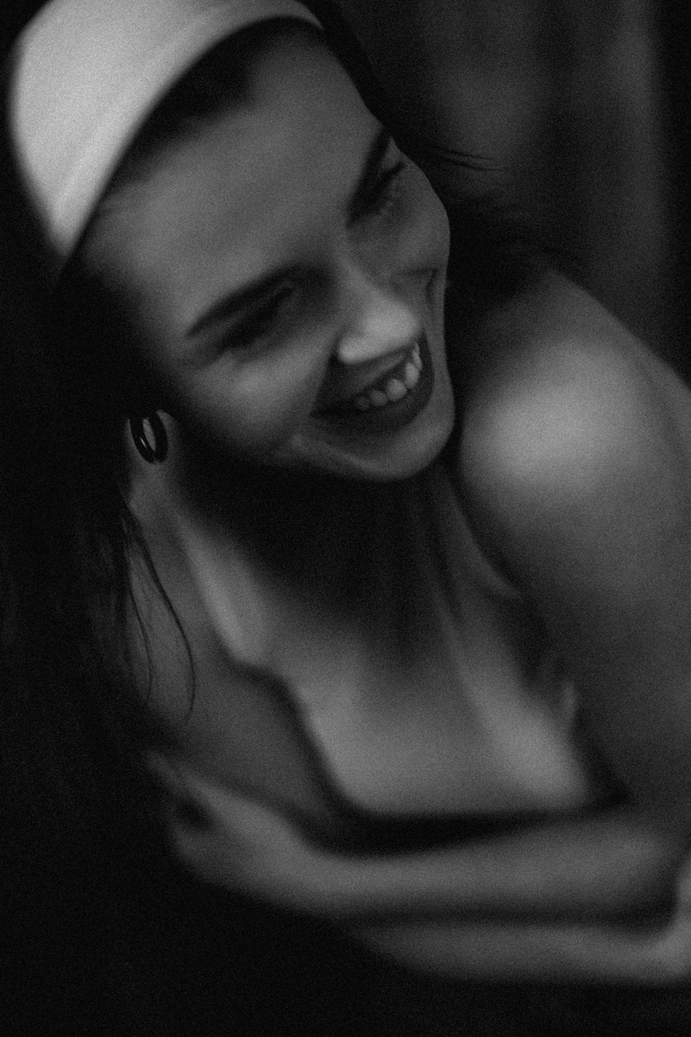 Portret uśmiechniętej kobiety z opaską na włosach, sfotografowanej w czerni i bieli, z widocznym fragmentem ramienia i delikatnym rozmyciem.