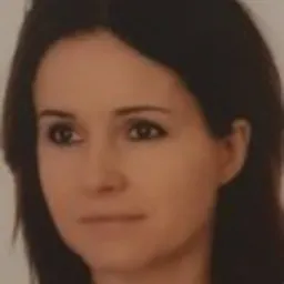 Portret kobiety o ciemnych włosach, z delikatnym uśmiechem, skierowana lekko w lewo, na rozmytym tle.