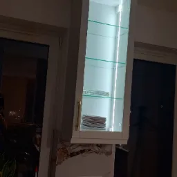 Podświetlana szafka wisząca z szklanymi półkami, na których ułożono talerze. Widoczne gniazdka elektryczne pod szafką.