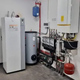 Kompletna instalacja grzewcza w kotłowni z kotłem, zbiornikiem buforowym, pompą ciepła i osprzętem, na podłodze leży pies rasy labrador.