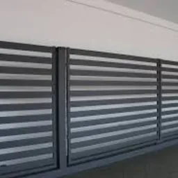 Nowoczesna, pozioma brama przesuwna z szarych, płaskich profili, na tle białej ściany z czerwonymi drzwiami w oddali.