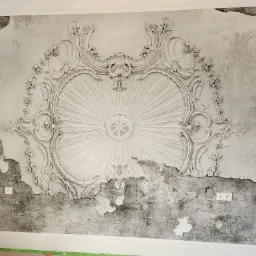 Ściana z dekoracyjną tapetą imitującą stiuk i efekt postarzenia, widoczne fragmenty odchodzącej tapety i gniazdka elektryczne.