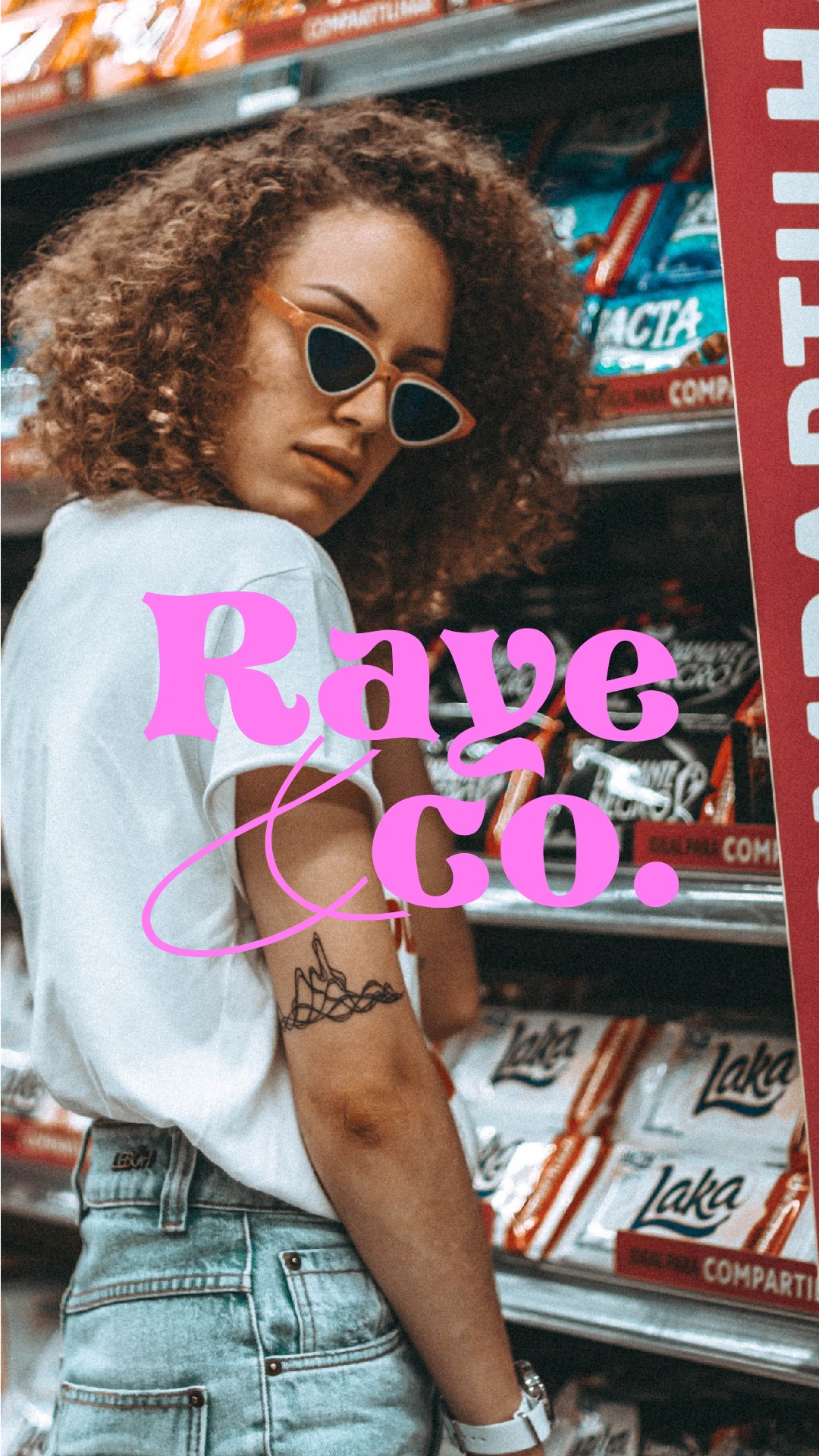 Kobieta z kręconymi włosami i okularami w kształcie trójkątów, odwrócona tyłem na tle półek sklepowych z przekąskami, z tatuażem na ramieniu i różowym logo 'Rave Co.' nałożonym na zdjęcie.