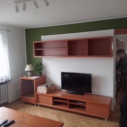 KOBRAStyle Maciej Wąsikowski - Pokój dzienny z drewnianą meblościanką, telewizorem, stolikiem kawowym i parkietem ułożonym w jodełkę; ściana pomalowana częściowo na zielono.