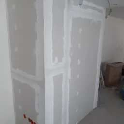 Konstrukcja z płyt gipsowo-kartonowych w trakcie szpachlowania, widoczne otwory pod gniazdka elektryczne, surowe wykończenie wnętrza.