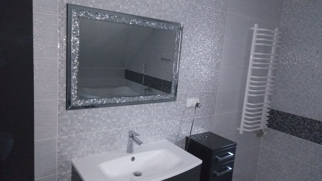 Wykończona łazienka w odcieniach szarości z błyszczącym lustrem w ozdobnej ramie, umywalką z szafką i grzejnikiem drabinkowym.