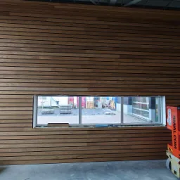 Ściana wykończona drewnianymi panelami z widocznym otworem okiennym, obok czerwony podnośnik nożycowy, widoczne elementy montażowe na podłodze.