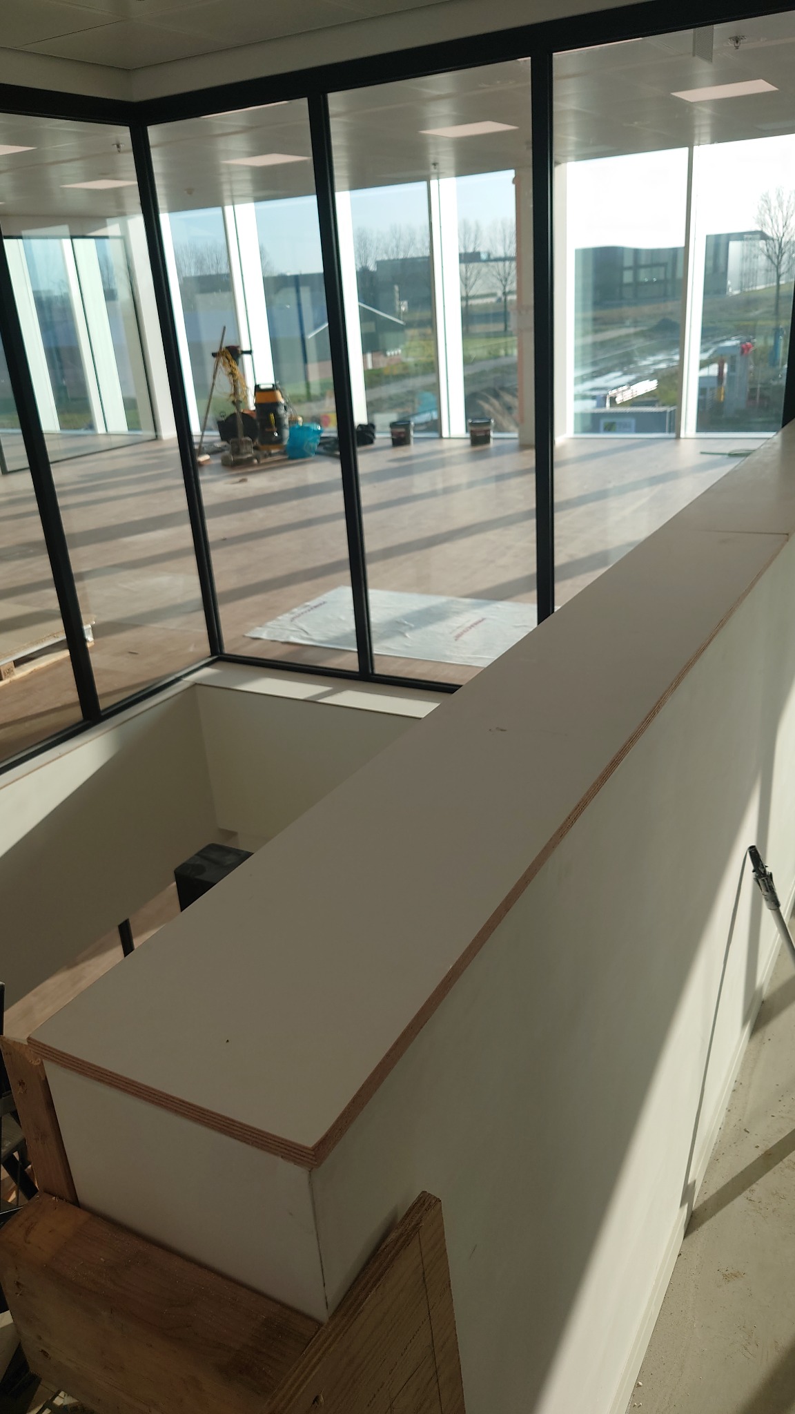 Montaż płyty karton gips na ścianie w nowoczesnym biurze z dużymi oknami, widoczne narzędzia i materiały budowlane.