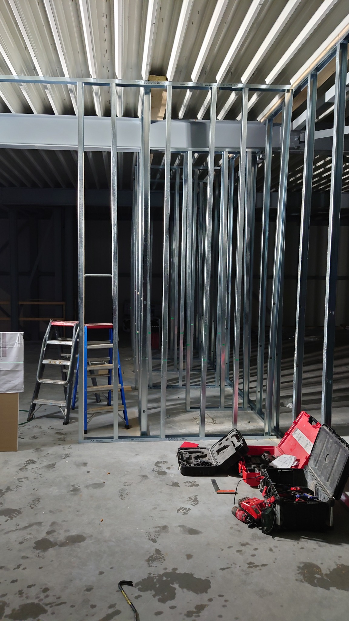 Konstrukcja szkieletowa z profili stalowych, widoczna drabina i skrzynki z narzędziami na betonowej posadzce w trakcie prac wykończeniowych.