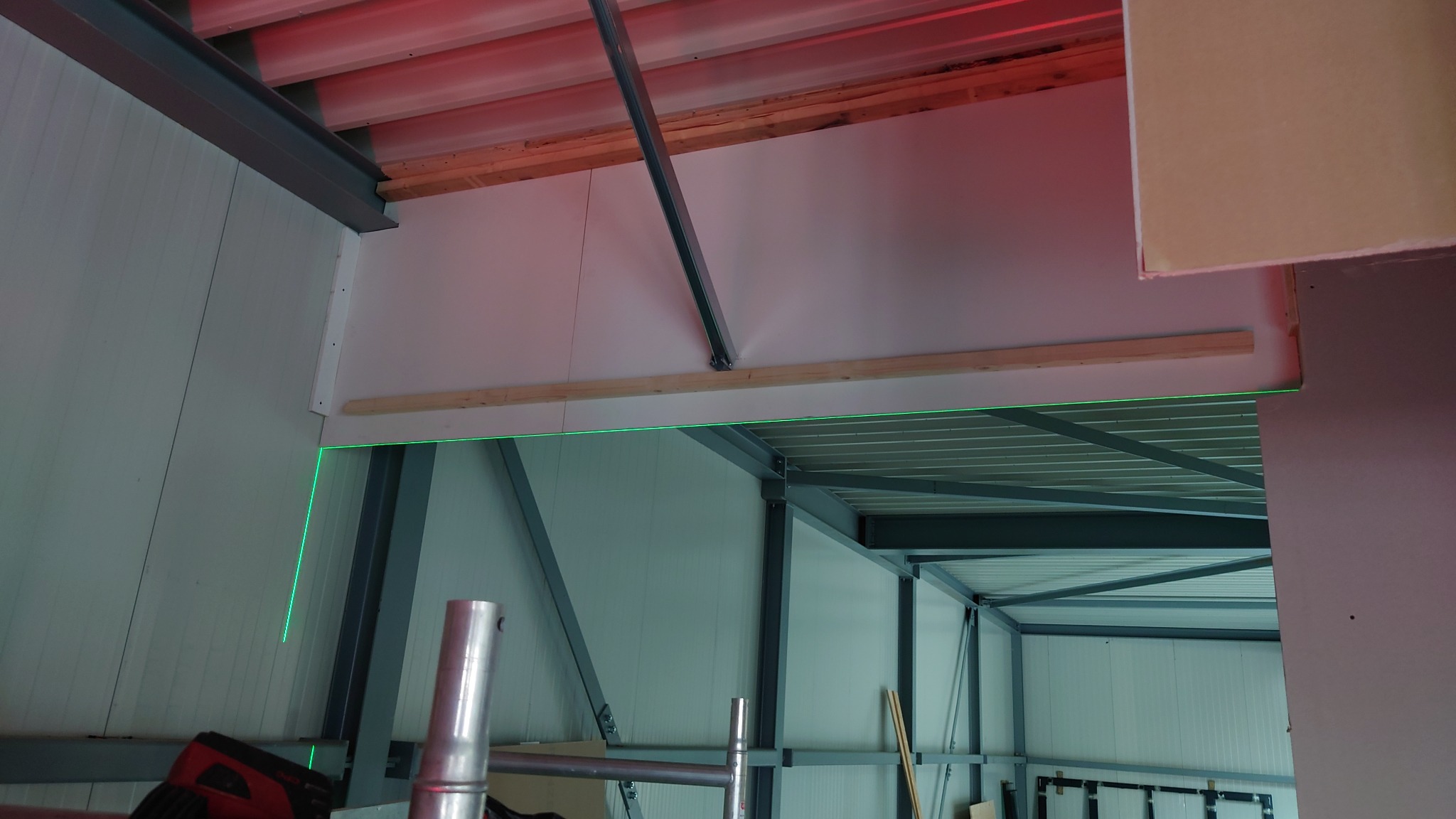 Montaż ścian działowych z użyciem lasera, widoczne profile stalowe konstrukcji budynku i fragment sufitu podwieszanego.