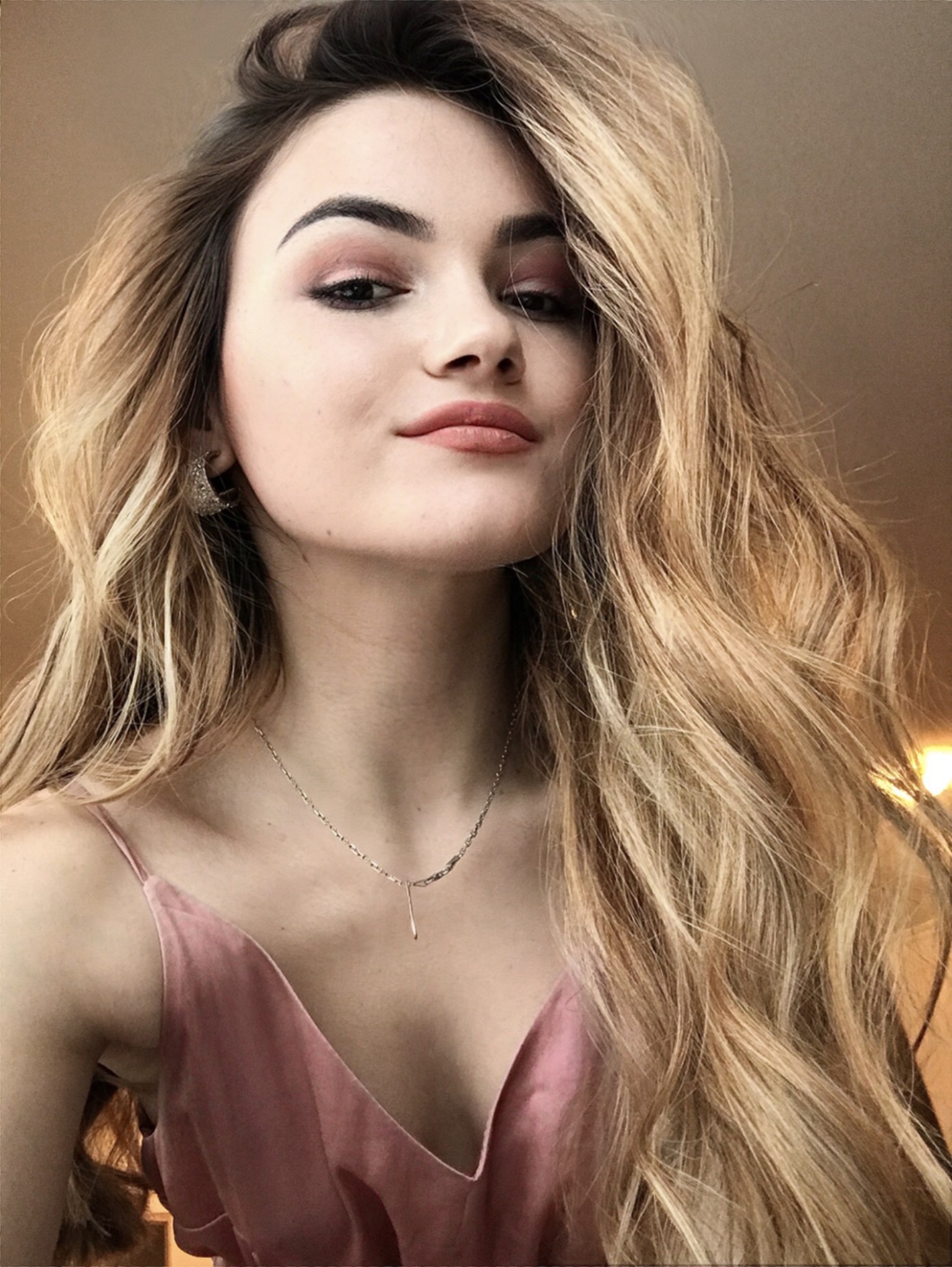 Portret młodej kobiety z blond włosami w różowej sukience na ramiączkach, z delikatnym makijażem i srebrną biżuterią