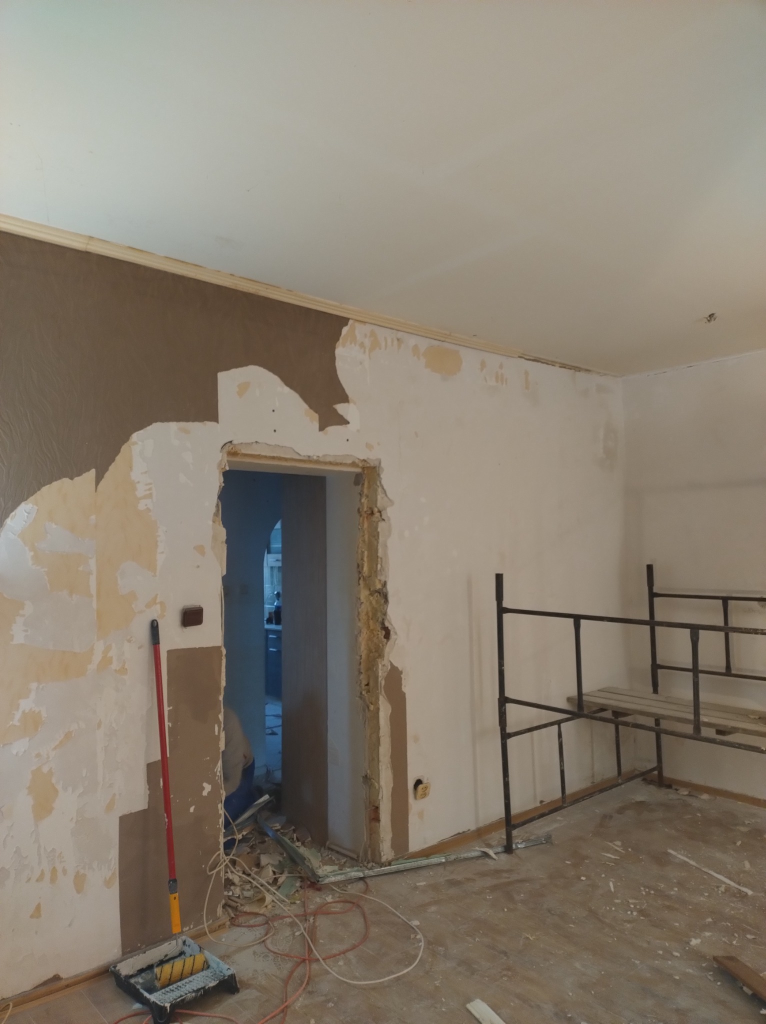 Demontaż tapety i przygotowanie ścian do malowania w trakcie remontu mieszkania. Widoczne rusztowanie, wałek malarski i resztki tapety.