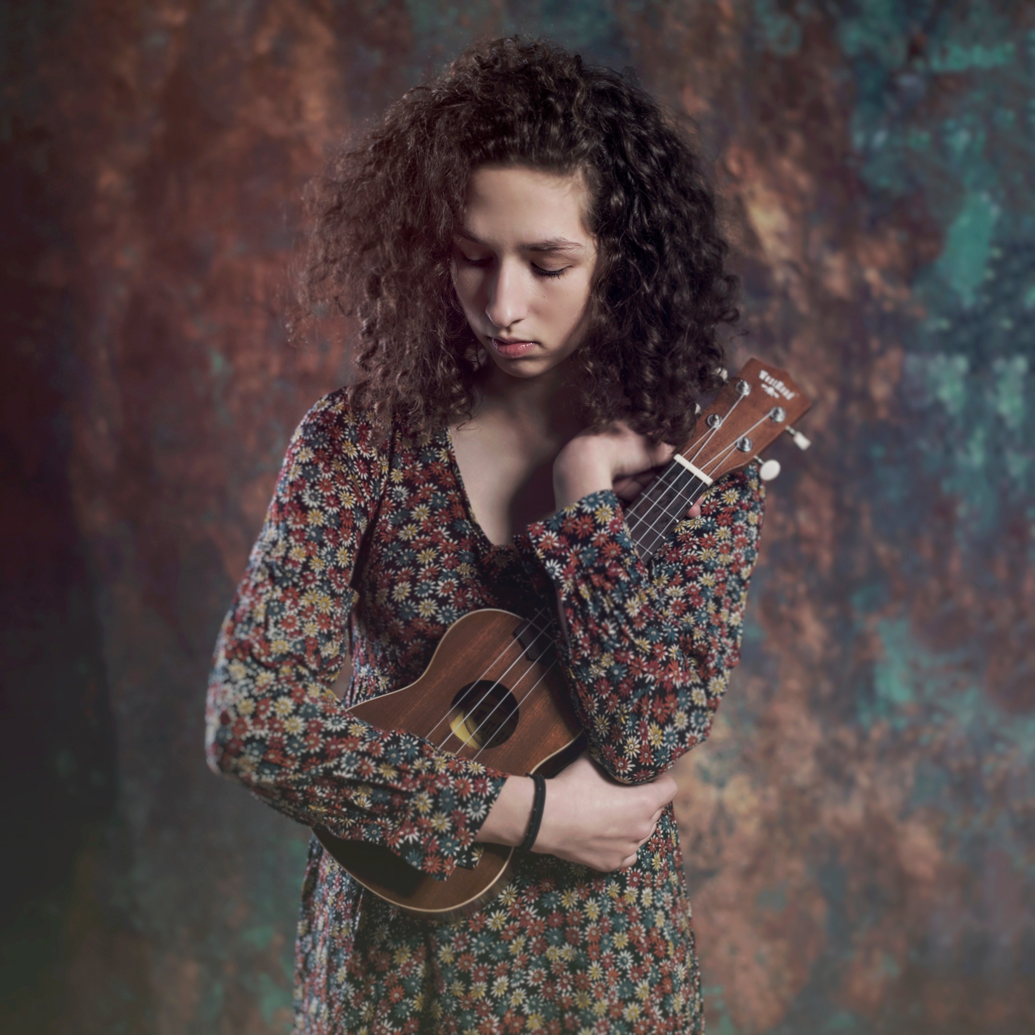 Portret młodej kobiety z kręconymi włosami, trzymającej ukulele na tle abstrakcyjnego tła w Gdyni.