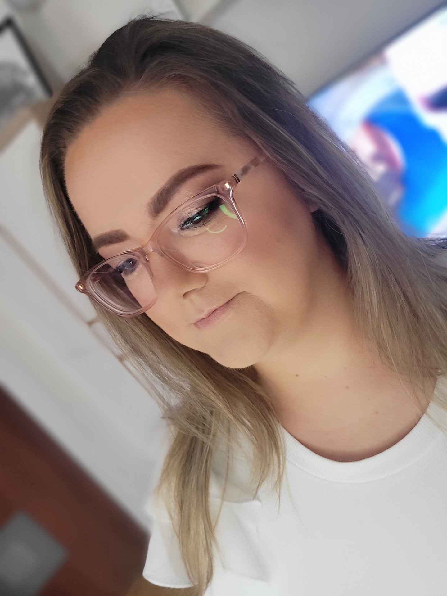 Portret kobiety w okularach z delikatnym, dziennym makijażem oczu w odcieniach brązu i zieleni, skierowanej wzrokiem w dół.