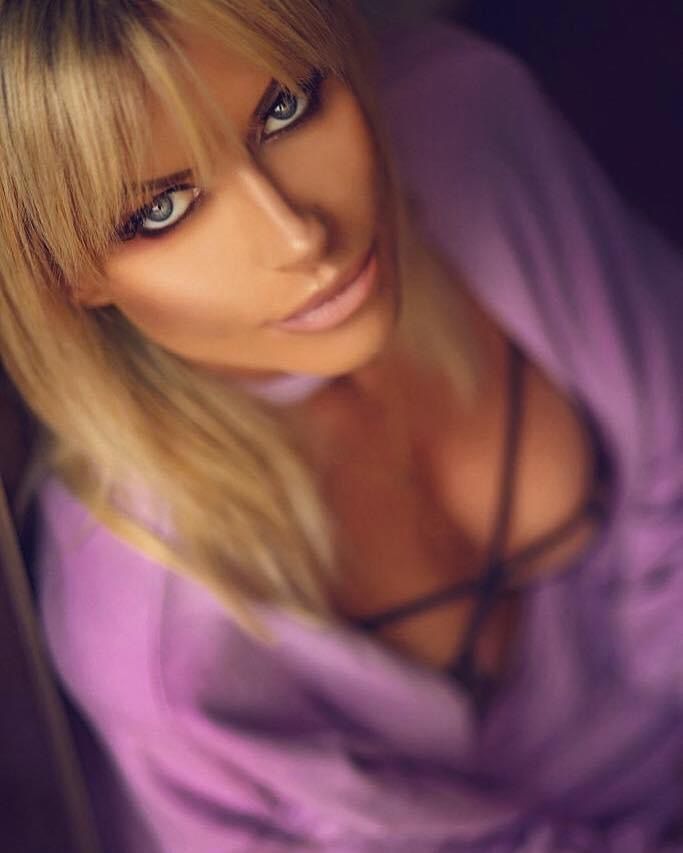 Portret kobiety z blond grzywką, intensywnym makijażem oczu i w fioletowej bluzce, ujęcie z góry.