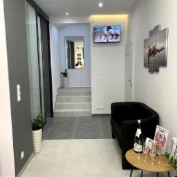 Wnętrze poczekalni kliniki z czarną sofą, stolikiem z szampanem i kieliszkami; na ścianie telewizor z prezentacją efektów zabiegów.