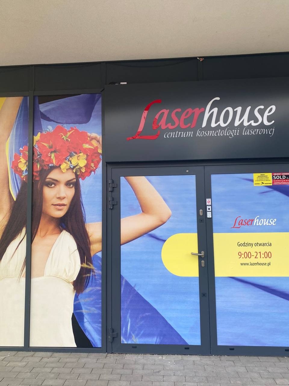 Wejście do salonu z szyldem 'Laserhouse centrum kosmetologii laserowej' oraz plakatem kobiety w wianku na tle ukraińskiej flagi.