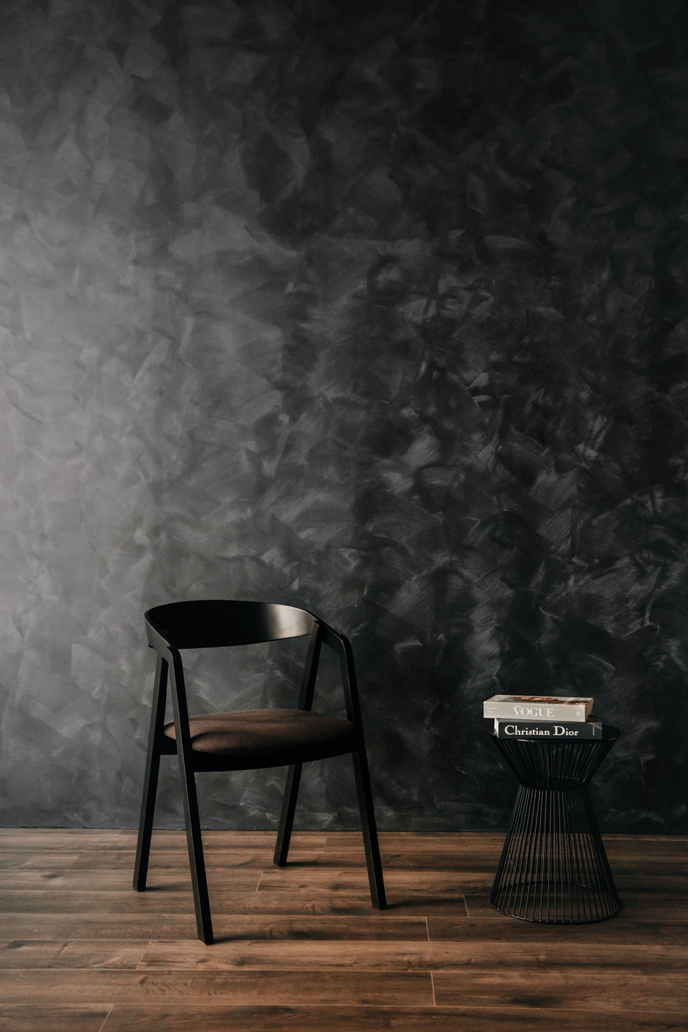 Minimalistyczne wnętrze: czarne krzesło i stolik z książkami na tle ściany z efektem dekoracyjnego tynku.