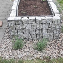 Dom i ogród Usługi Krystian Kłonowski - Gabionowa rabata kwiatowa z lawendą, obłożona korą, na tle kostki brukowej i trawnika.