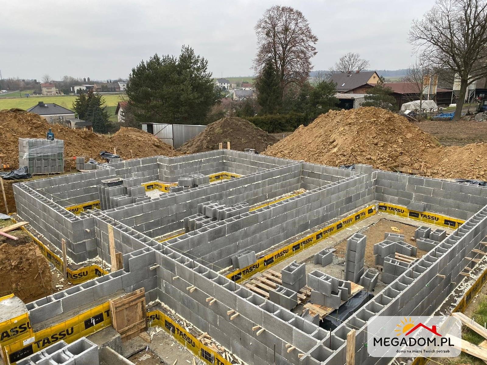 Wykop i murowane ściany fundamentowe z bloczków betonowych z izolacją przeciwwilgociową w Rybniku, widok z góry na plac budowy przed zasypaniem.