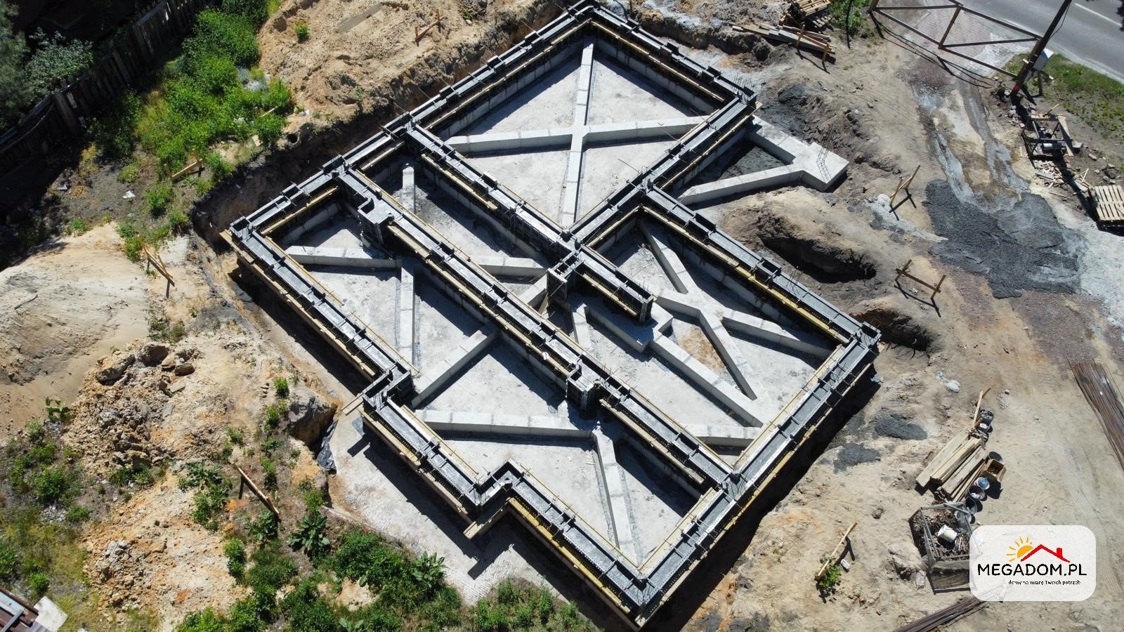 Zalane betonem szalunki fundamentów domu jednorodzinnego, widok z drona na plac budowy w słoneczny dzień.