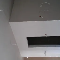 Świeżo wykończony sufit podwieszany z otworami na oświetlenie i wystającymi kablami, gotowy do dalszych prac wykończeniowych.