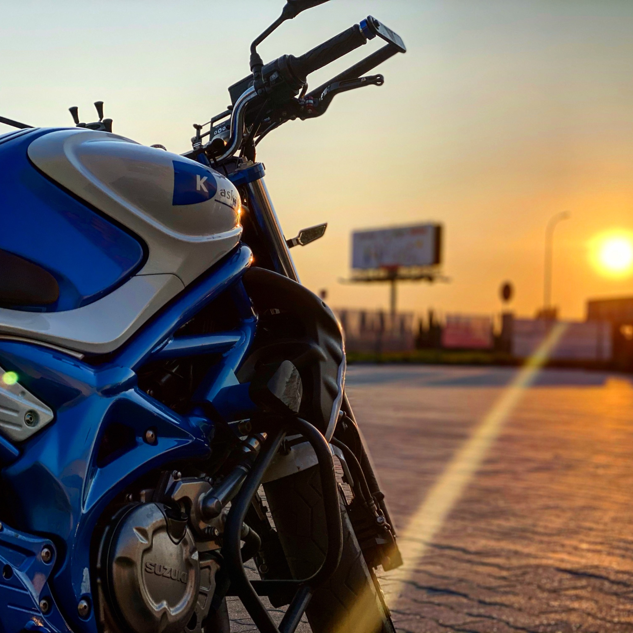 Błękitno-biały motocykl Suzuki na tle zachodzącego słońca i billboardu reklamowego, widok z dołu.