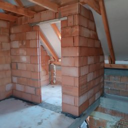 Marcin Skrętkowicz Usługi Ogólnobudowlane - Wnętrze poddasza w trakcie budowy: ściany z czerwonej cegły, drewniana konstrukcja dachu, widoczny strop. Etap murowania ścian działowych.