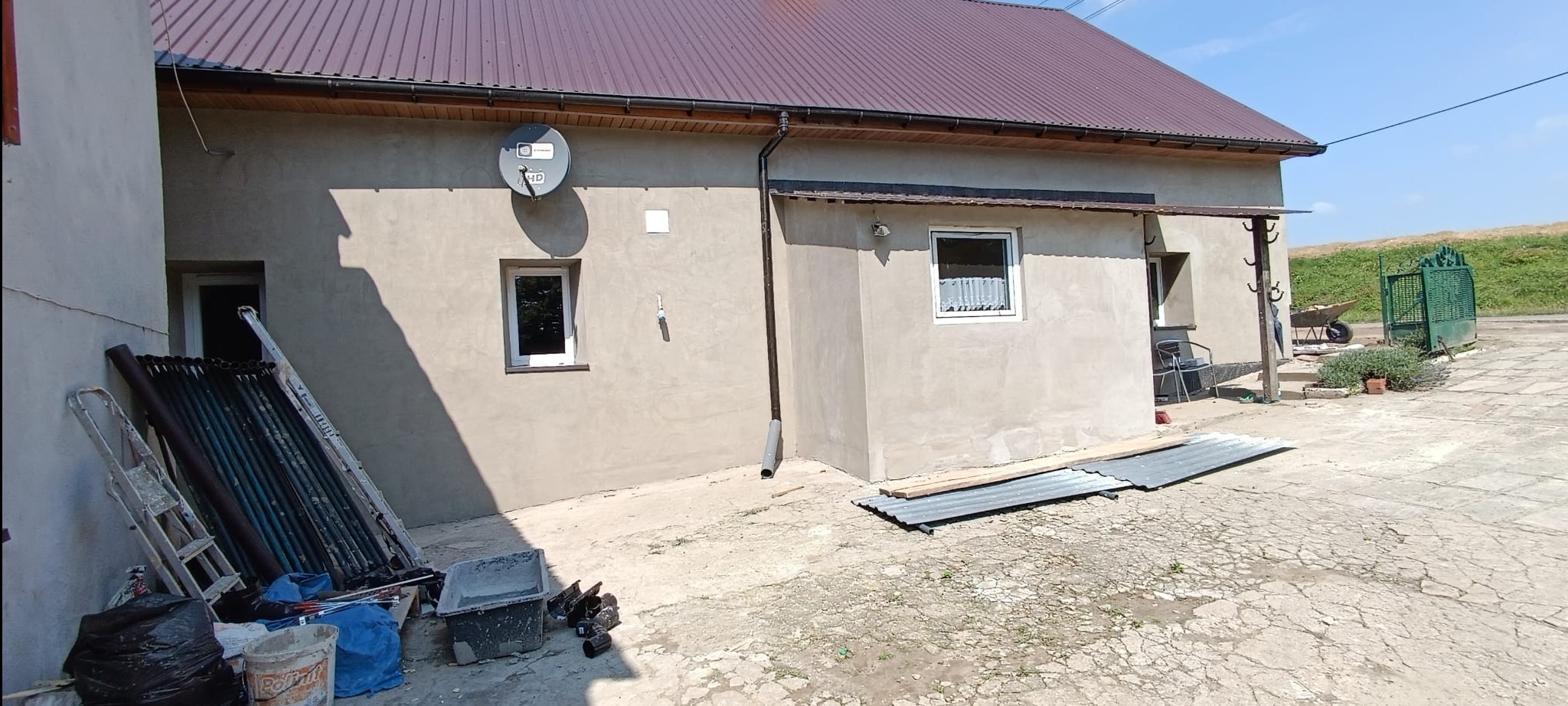 Budynek z nową elewacją w trakcie prac wykończeniowych, widoczne rusztowania, drabiny, narzędzia i materiały budowlane.