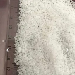 Zbliżenie białych granulek substancji sypkiej, z widoczną podziałką centymetrową na boku, sugerującą pomiar wielkości granulek.