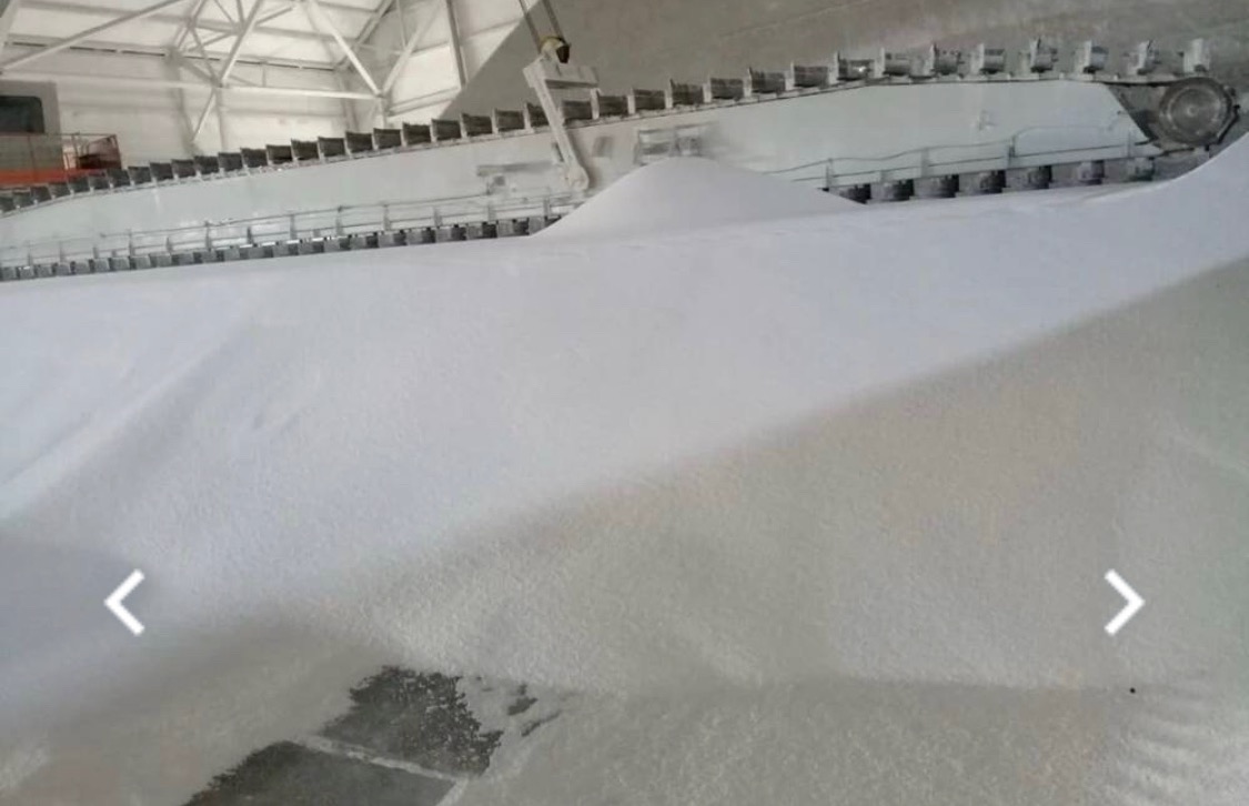 Magazyn nawozów z widoczną taśmą transportującą i górą białego granulatu.