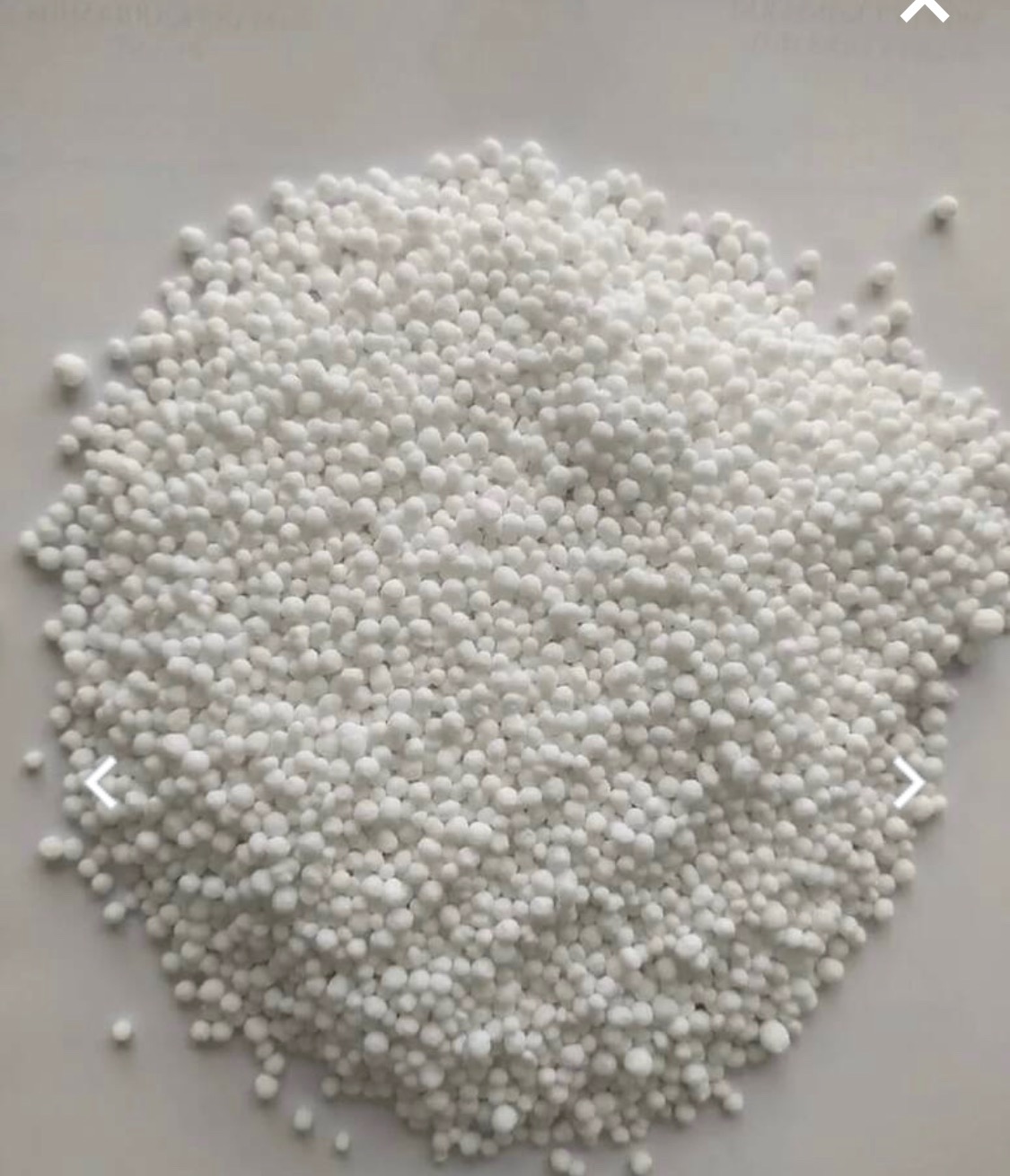Białe granulki nawozu mineralnego ułożone w nieregularny stos na jasnym tle.